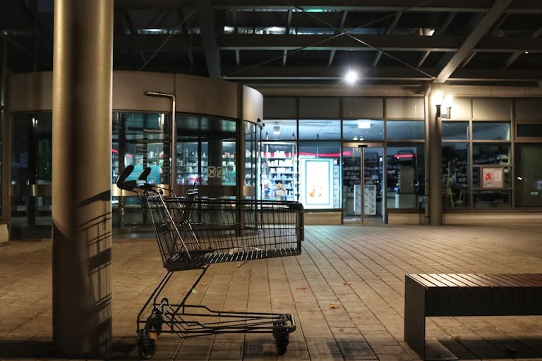 A lone shopping cart outside a storefront at night, under urban lighting.