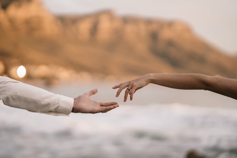 Two hands reaching towards each other against a scenic blurred background.